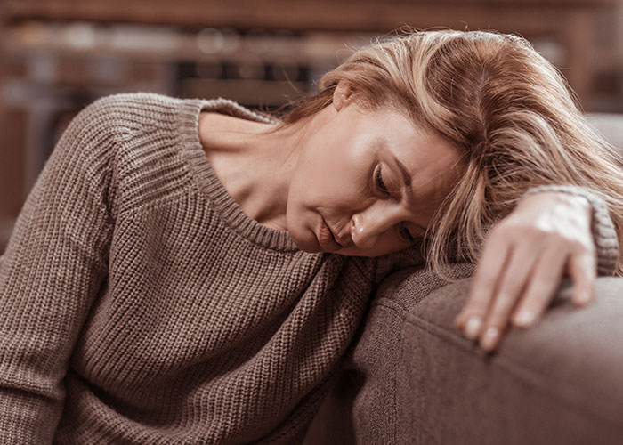 Sad single woman resting head on couch arm, reflecting on reasons many single women avoid men like the plague.