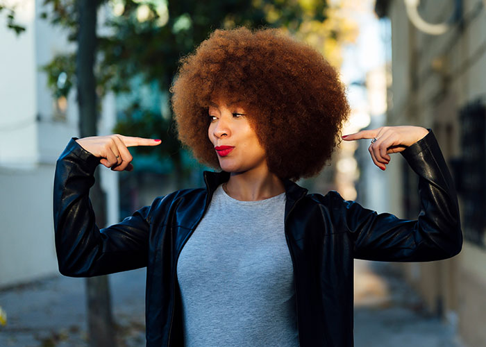 Young woman with afro hairstyle wearing a leather jacket confidently pointing to herself outdoors, representing single women avoiding men.