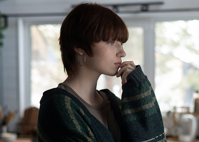 Young woman with short hair and hoop earrings, wearing a sweater, looking thoughtful and avoiding men like the plague.