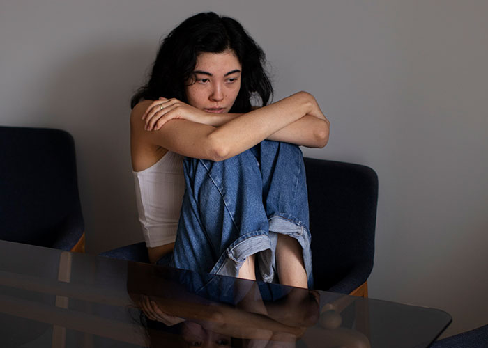 Young woman sitting alone in a chair, looking contemplative and distant, reflecting on why single women avoid men.