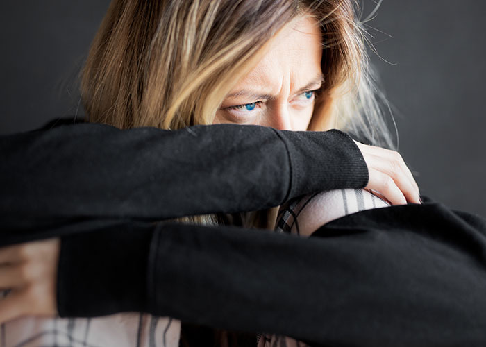 Woman with a troubled expression, hiding her face in her arms, reflecting on why single women avoid men like the plague.