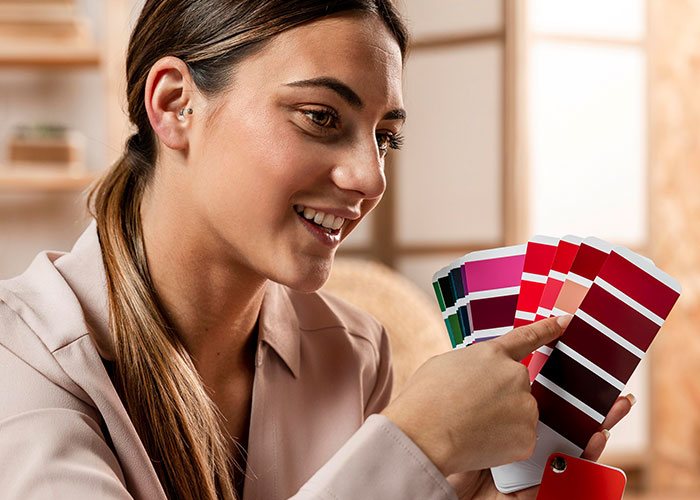 Young woman smiling and holding colorful paint swatches while selecting shades in a bright indoor space, single women concept.