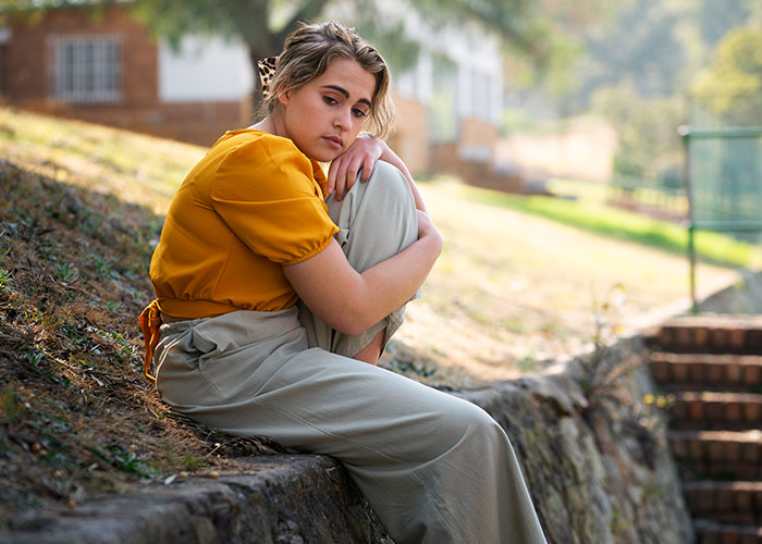 Young single woman in an orange blouse sitting alone outdoors, reflecting on why single women avoid men like the plague.