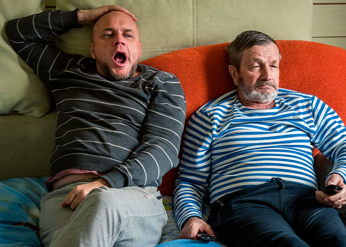 Two men sitting on a couch, one yawning and the other looking bored, illustrating reasons single women avoid men.