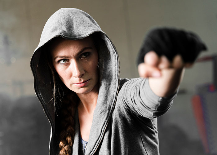 Woman in gray hoodie with braided hair throwing a punch in a boxing gym, representing single women avoiding men.