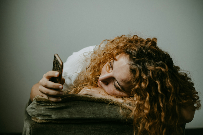 Young woman with curly hair resting on a couch, looking at her phone, reflecting on generational trauma conversation. - 13