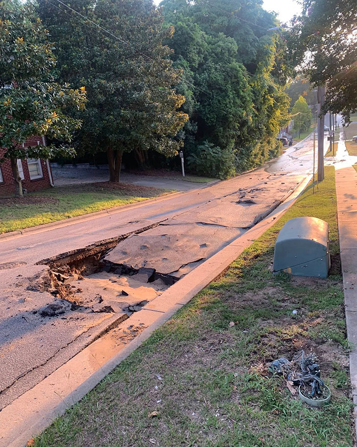 Damaged road with a large sinkhole causing disruption in a residential neighborhood, illustrating instant karma for ignoring warnings.