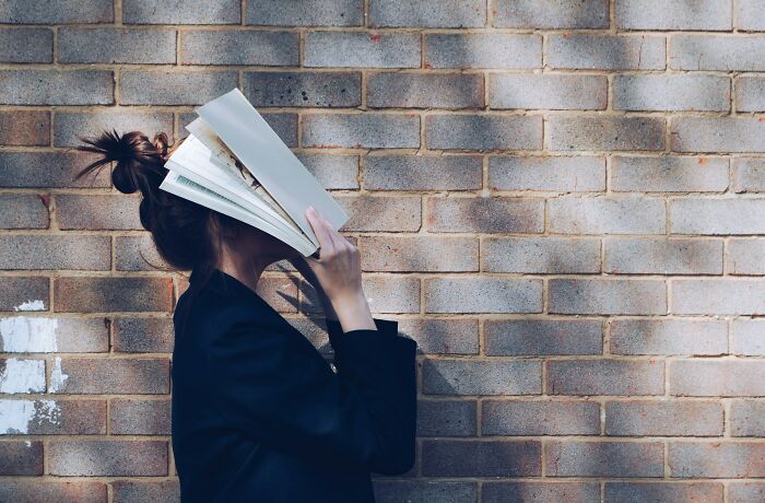 Person holding open book in front of their face standing against a textured brick wall, illustrating lies proven false.