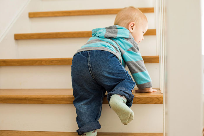 Toddler climbing wooden stairs in a home, related to woman getting a CPS visit after sibling reports unsafe loft concerns. - 1