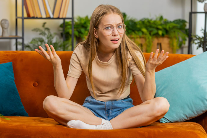 Young woman frustrated with sibling behavior sitting on couch, contemplating moving out for peace and independence. - 7