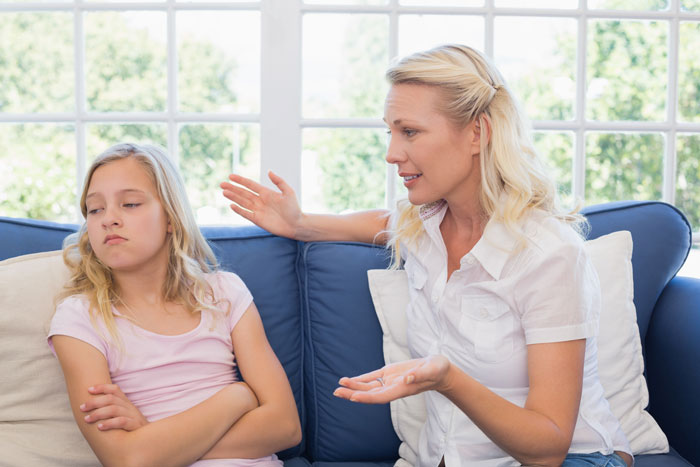 Teen girl sitting with arms crossed, ignoring a woman trying to talk, showing sibling tension and conflict at home. - 19