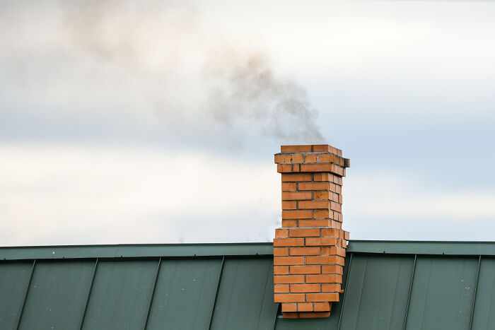Brick chimney on a green roof with smoke rising, related to people who deal with dead bodies and unsettling details.