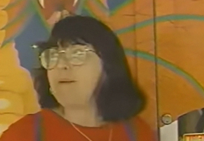 Woman with glasses and dark hair standing in front of a colorful mural related to gaming store sword sales closure. - 20
