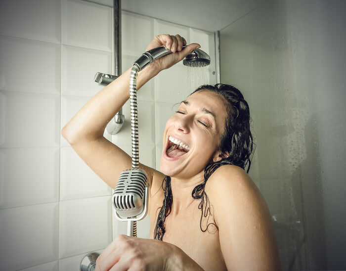 Woman singing joyfully in the shower holding a showerhead and a microphone, illustrating hilarious wrong person stories. - 15