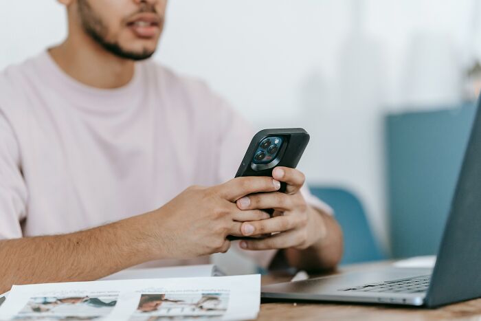 Man holding smartphone near laptop, illustrating mortifying stories of people sending messages to wrong recipients. - 23