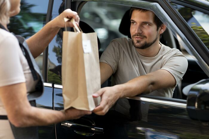 Man in car receiving a paper bag from a woman, illustrating mortifying stories of sending items to the wrong person. - 18