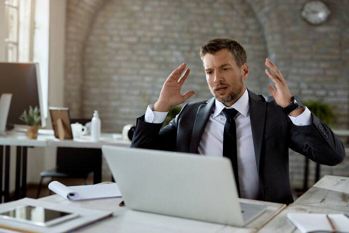 Businessman in suit reacting with shock at laptop, illustrating mortifying stories of sending messages to wrong person. - 16