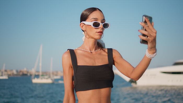 Young woman wearing sunglasses taking a selfie near a marina, illustrating stories of sending something to the wrong person. - 29