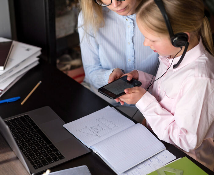 Woman and child with headset looking at phone, illustrating mortifying stories of sending messages to the wrong person. - 8