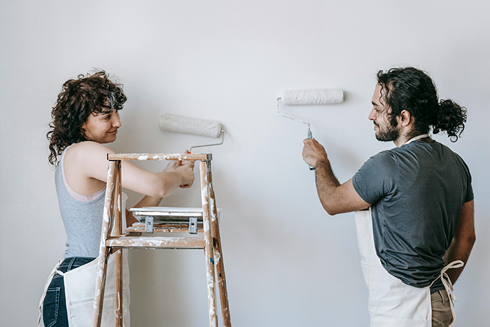 Couple painting a wall together, representing a wife discovering her husband secretly owns and rents his mom&rsquo;s house.