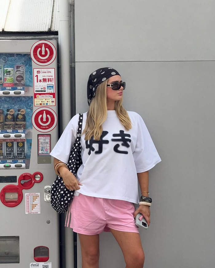 Australian influencer wearing sunglasses and polka dot headscarf posing beside a vending machine during Japan trip.