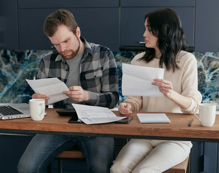 Couple reviewing bills at kitchen table, showing concern about the cost of passports for wife and kids. - 5