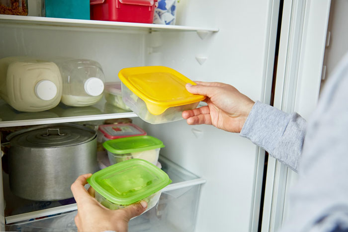 Person placing food containers with yellow and green lids inside a refrigerator as part of a theft prevention story. Person placing food containers with yellow and green lids inside a refrigerator as part of a theft prevention story.