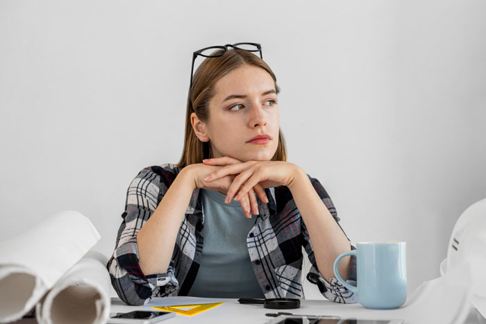 Young woman at desk looking away thoughtfully, relating to story of adding menstrual blood to food to prevent theft. Young woman at desk looking away thoughtfully, relating to story of adding menstrual blood to food to prevent theft.