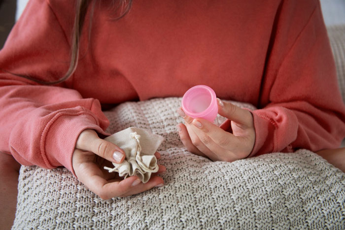 Person in a red sweater holding a pink menstrual cup and a cloth, representing menstrual blood prevention methods. Person in a red sweater holding a pink menstrual cup and a cloth, representing menstrual blood prevention methods.