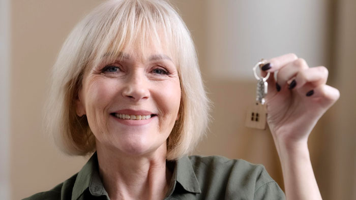 Smiling woman holding house keys, symbolizing the concept of stealing daughters trust fund in a home setting.