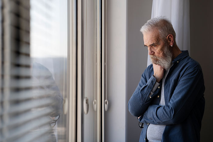 An elderly man with a gray beard standing pensively by a window, reflecting on a gold digger lesson. - 1