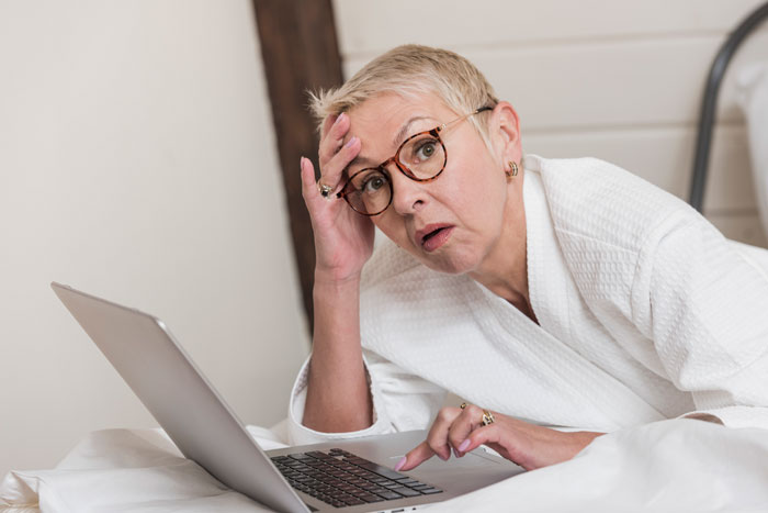 Woman in white robe looking shocked and upset while using a laptop, reflecting toxic family and stepsis conflict. - 15