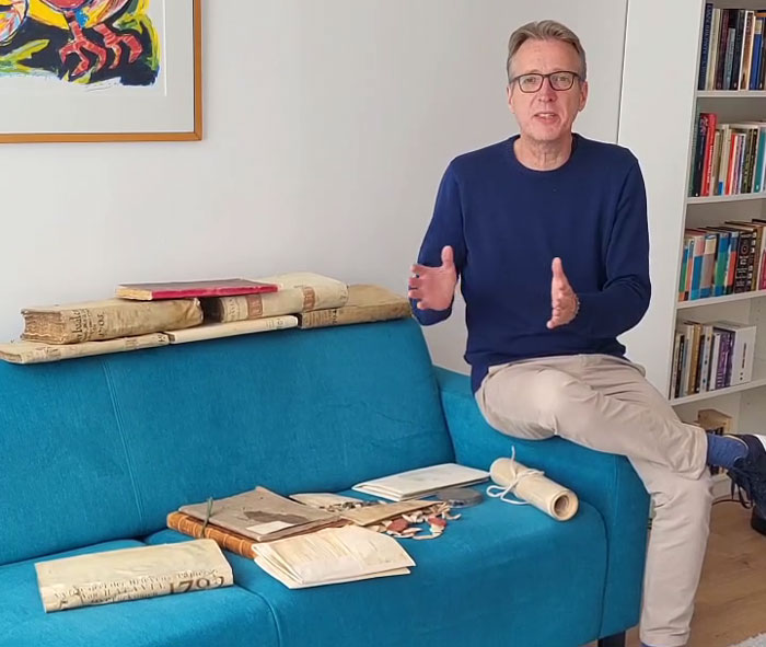 Man in glasses sitting next to stolen historic documents spread on a blue couch, discussing the documents' resurfacing. - 3