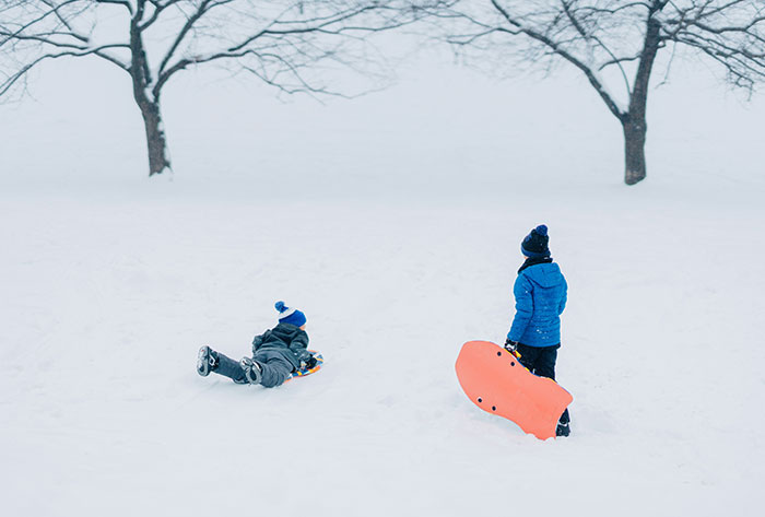 Two children playing in the snow with sleds, capturing childhood moments related to messed up stories keyword.