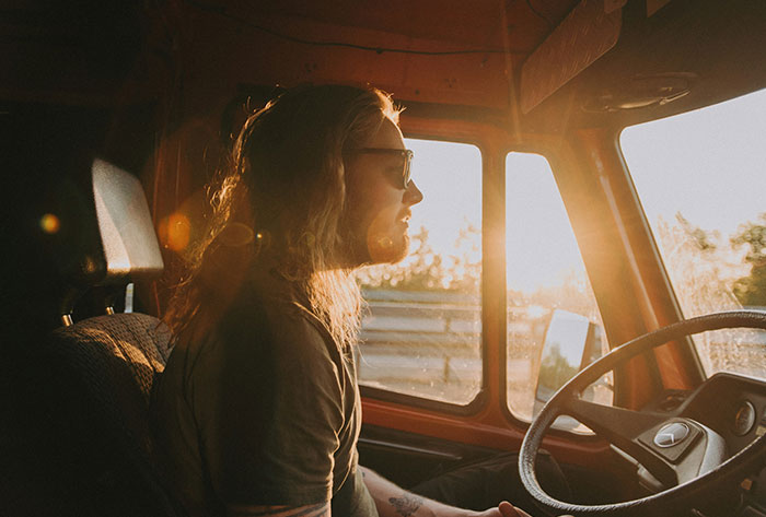 Person with long hair and glasses driving at sunset, reflecting on childhood memories that were really messed up.