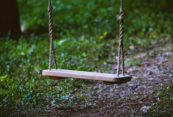 Empty wooden swing hanging by ropes in a quiet outdoor setting, evoking childhood memories and messed up stories.