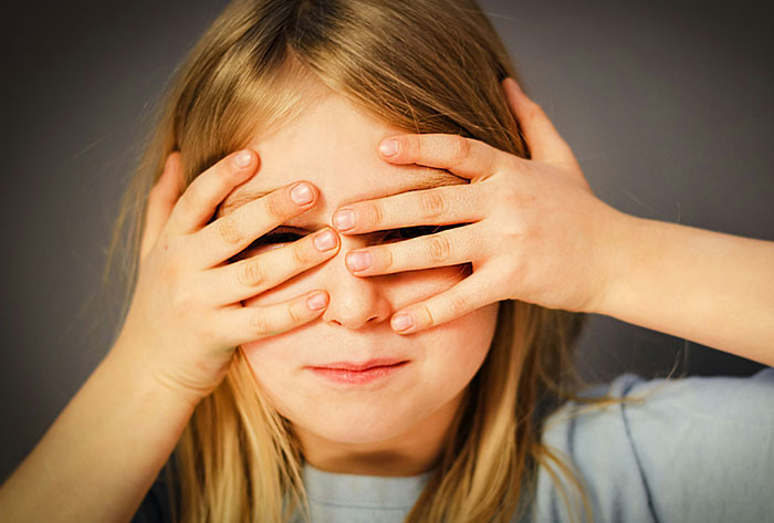 Young girl covering her eyes with both hands, illustrating childhood moments from stories that were really messed up.