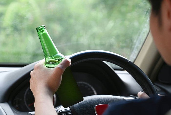 Person holding a green bottle while driving a car, illustrating a messed up childhood story related to risky behavior.