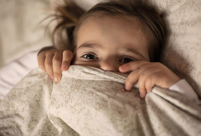 Young child peeking from under bed covers, representing childhood stories and moments people didn’t realize were messed up.