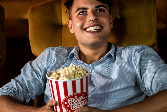 Young man smiling while holding popcorn, enjoying a movie, illustrating childhood moments and stories.