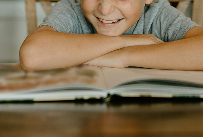 Smiling child leaning on arms with an open book in front, illustrating stories from people's childhood experiences.