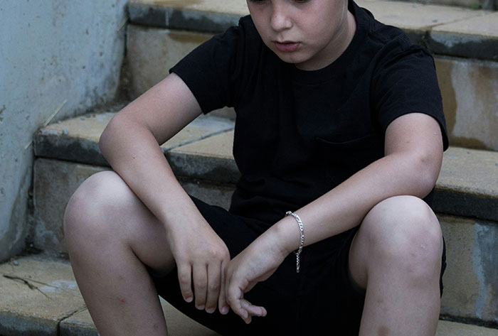 Sad child sitting on outdoor steps, reflecting on childhood stories and difficult memories from their past.