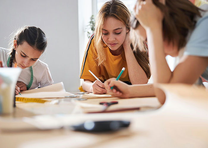 Three students focused on writing at a table, highlighting common issues people were punished for at school. - 22