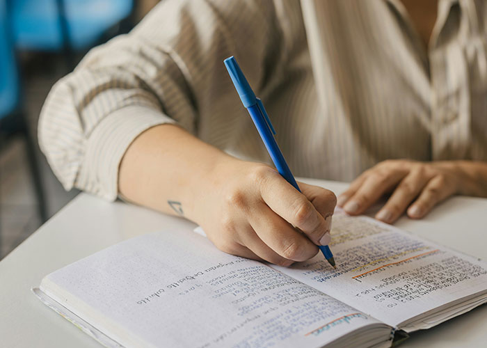 Close-up of person writing in a notebook with a blue pen, reflecting on school punishments and related memories. - 30