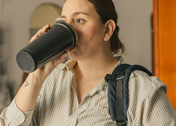 Young woman with backpack drinking from a black cup, reflecting on school punishments people are still upset about. - 25