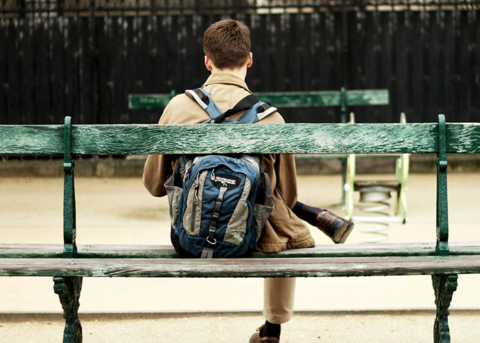 Student sitting on a green bench with a backpack, reflecting on things punished at school that still upset people today. - 31