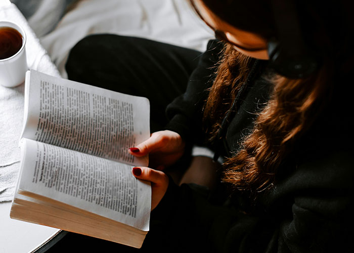 Person reading a book indoors near a cup of tea, reflecting on things people were punished for at school. - 8