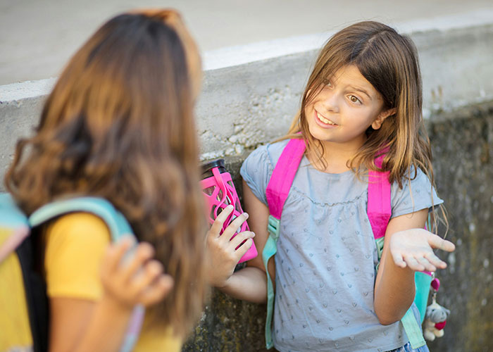 Two schoolgirls with backpacks talking outside, showing expressions related to being upset about school punishments. - 17