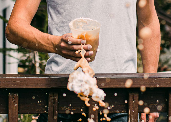 Person spilling drink from a plastic cup over a wooden railing, highlighting things punished at school. - 4