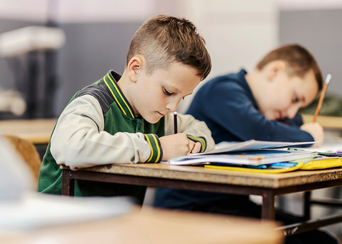 Two young boys focused on writing at their school desks, illustrating moments related to punishment at school. - 20